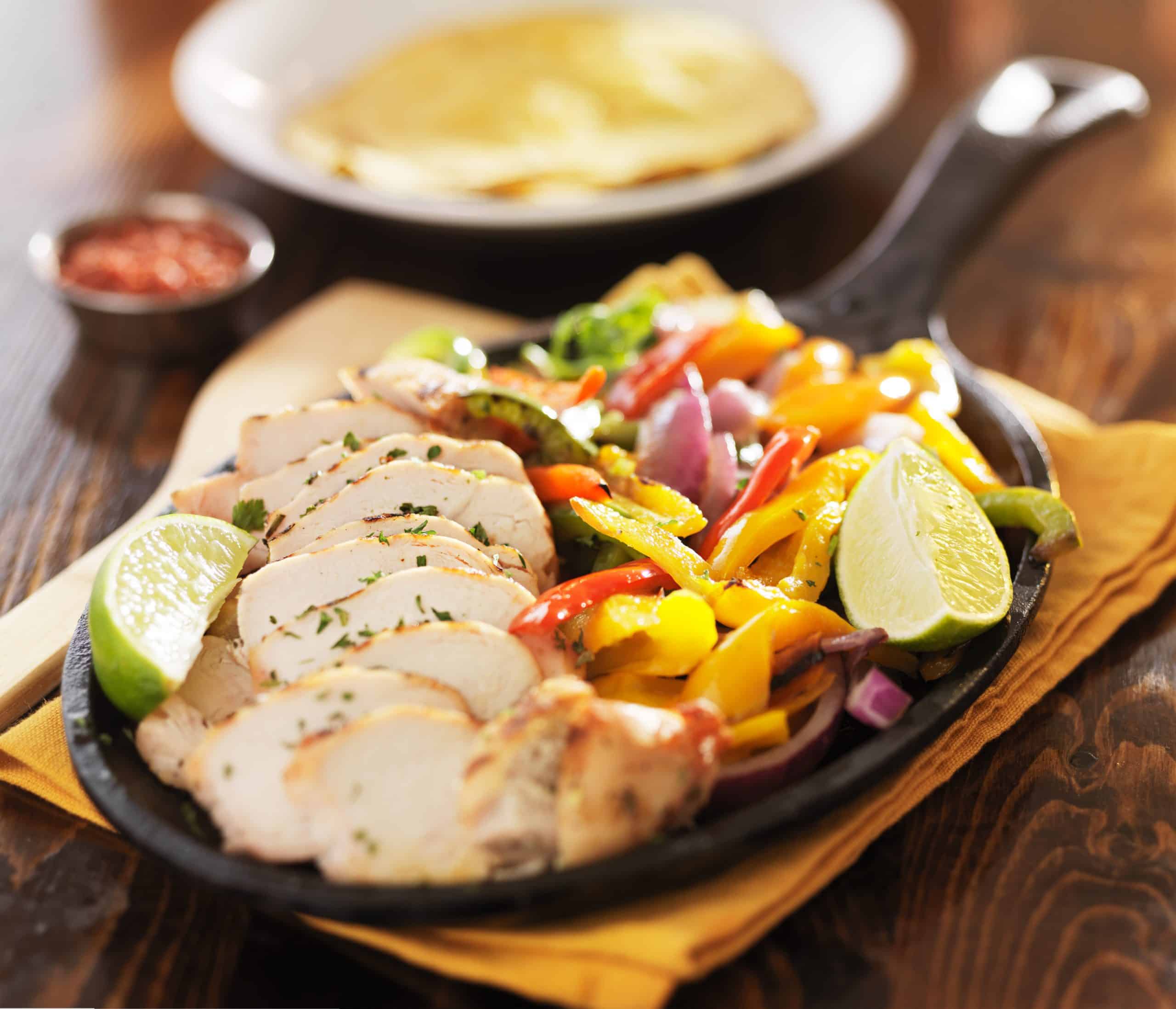 grilled mexican chicken fajita skillet meal on wooden table top with beer in background